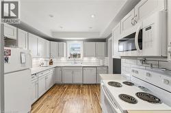 The kitchen features white cabinetry, white appliances, a white subway tile backsplash, and wood flooring - 
