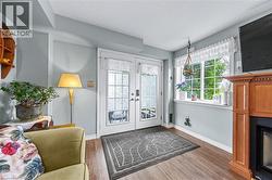 Living area featuring light wood flooring, a fireplace with a light wood mantel, a window providing natural light, and double glass doors - 