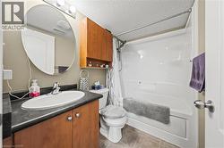 The bathroom features a vanity with a dark countertop and wood cabinetry, an oval mirror, and a full bathtub with shower - 