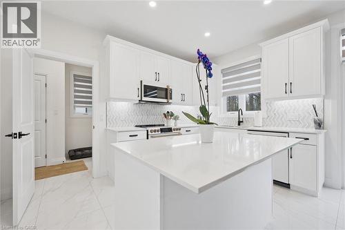 Modern kitchen featuring a large central island with a solid surface countertop, white shaker-style cabinetry, stainless steel appliances, a chevron-patterned tile backsplash, and recessed lighting - 213 Fallowfield Drive, Kitchener, ON - Indoor Photo Showing Kitchen With Upgraded Kitchen