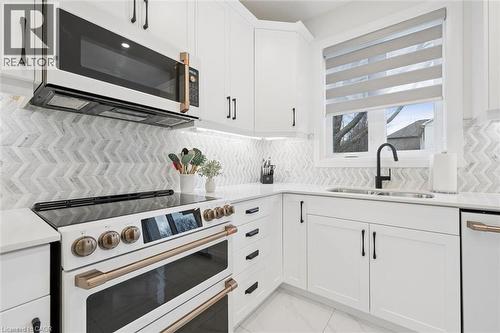 Contemporary kitchen featuring white cabinetry with matte black hardware, a chevron pattern tile backsplash, and light-tone countertops - 213 Fallowfield Drive, Kitchener, ON - Indoor Photo Showing Kitchen With Double Sink With Upgraded Kitchen