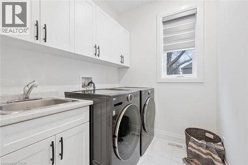 Dedicated laundry room featuring white cabinetry with matte black hardware, an integrated utility sink with a chrome faucet, a stone-finish countertop, and a window for natural light - 213 Fallowfield Drive, Kitchener, ON - Indoor Photo Showing Laundry Room