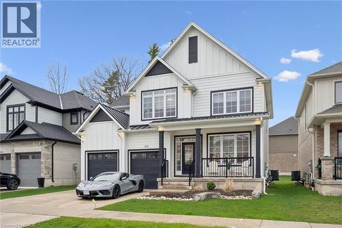 Modern farmhouse-style residence featuring white vertical siding, black trim accents, a prominent front porch with dark pillars and railings, a paved driveway, and an attached two-car garage with dark - 213 Fallowfield Drive, Kitchener, ON - Outdoor With Facade