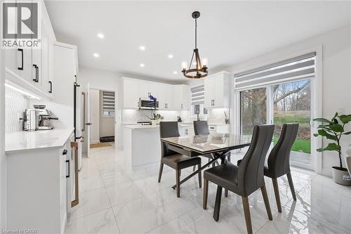 Bright kitchen and dining area featuring white cabinetry, a patterned tile backsplash, and light-toned flooring - 213 Fallowfield Drive, Kitchener, ON - Indoor