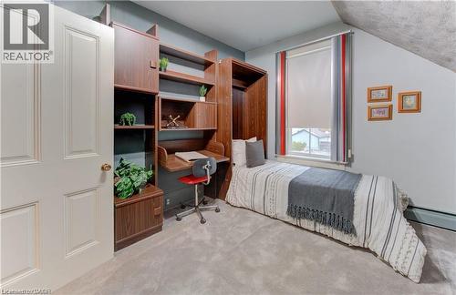 This room features a built-in wooden desk and shelving unit, a window with a roller blind, and light gray carpet flooring - 48 Dupont Street, Waterloo, ON - Indoor Photo Showing Bedroom