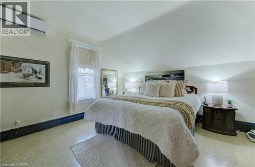 This inviting room features a window with white curtains, a wall-mounted air conditioning unit, and a bed with a decorative headboard - 48 Dupont Street, Waterloo, ON - Indoor Photo Showing Bedroom