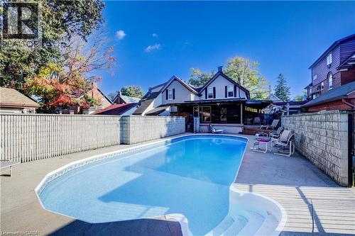 The property features a large outdoor swimming pool with an integrated spa area and a surrounding concrete patio - 48 Dupont Street, Waterloo, ON - Outdoor With In Ground Pool