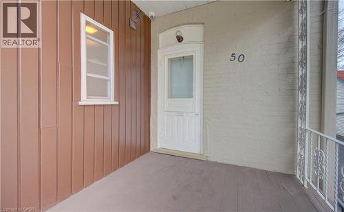 The property features a front porch with a white entry door, an exterior wall with vertical brown siding, and a white-framed window - 48 Dupont Street, Waterloo, ON - Outdoor With Exterior