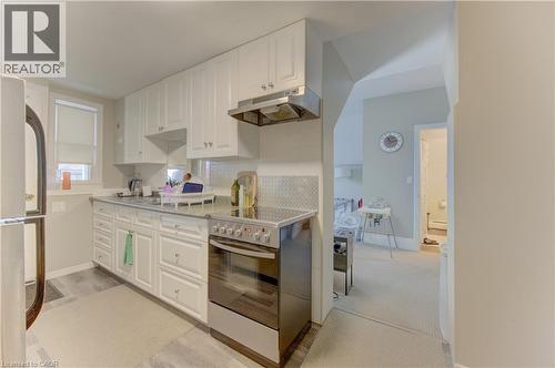 The kitchen features white cabinetry, a stainless steel oven with a matching range hood, and a light-colored backsplash - 48 Dupont Street, Waterloo, ON - Indoor Photo Showing Kitchen