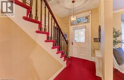 The inviting entry features a staircase with a wooden banister, a red carpet runner, and a front door with a stained glass transom window - 