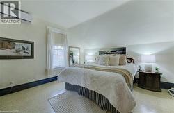 This inviting room features a window with white curtains, a wall-mounted air conditioning unit, and a bed with a decorative headboard - 