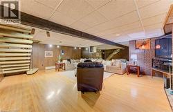 Spacious recreation room featuring light wood flooring, wood paneled walls, exposed wooden beams, and a brick accent wall with a built-in shelf - 