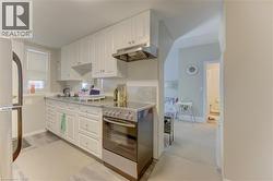 The kitchen features white cabinetry, a stainless steel oven with a matching range hood, and a light-colored backsplash - 