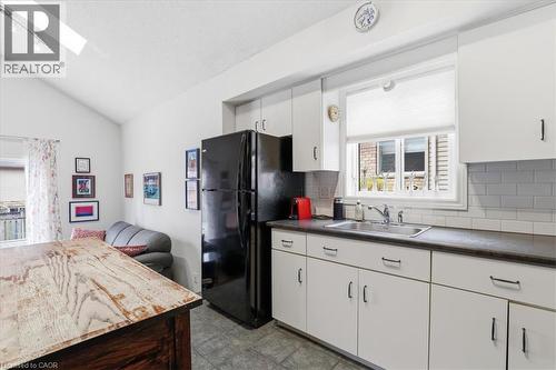 The kitchen features white cabinetry with dark pulls, a black refrigerator, and a window above the sink - 110 Milton Avenue, Cambridge, ON - Indoor Photo Showing Kitchen