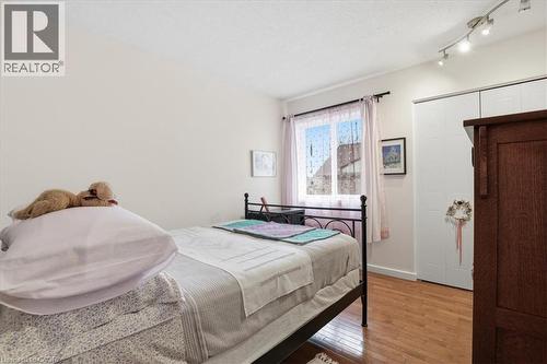 This room features hardwood floors, a window with sheer curtains, track lighting, and a white closet with sliding doors - 110 Milton Avenue, Cambridge, ON - Indoor Photo Showing Bedroom