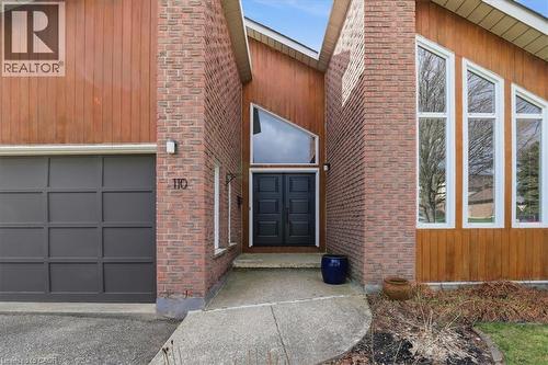 The property features a brick and wood facade, a prominent dark gray garage door, and a double entry door with an overhead triangular window - 110 Milton Avenue, Cambridge, ON - Outdoor With Exterior