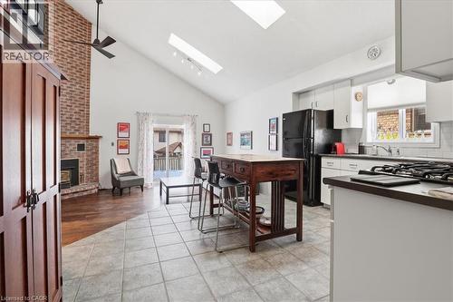 Spacious open concept living area featuring a vaulted ceiling with skylights, a brick fireplace, and a kitchen with white cabinetry, a gas range, and a black refrigerator - 110 Milton Avenue, Cambridge, ON - Indoor Photo Showing Kitchen