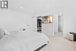Bright bedroom with recessed lighting, light-toned carpeting, a built-in closet with shelving, and a wall-mounted television - 