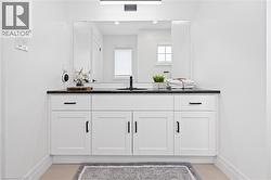 Modern bathroom vanity featuring white shaker cabinetry with black hardware, a dark countertop, an undermount sink with a matte black faucet, and a large mirror - 