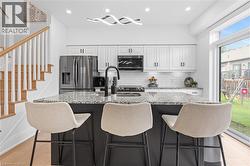 Modern kitchen featuring a black island with a speckled countertop, white cabinetry with black hardware, and stainless steel appliances - 