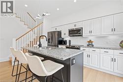 Modern kitchen featuring a central island with a sink, white cabinetry, integrated stainless steel appliances, and wood-finish flooring - 