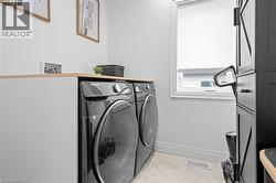 Dedicated laundry area featuring a light wood-finish countertop, white walls, light-toned floor tiling, and a window with a privacy blind - 