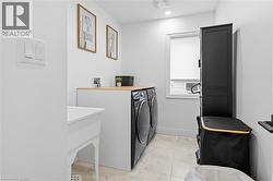 Functional laundry area featuring light-toned tile flooring, a utility sink, and a countertop with wood-finish surface - 