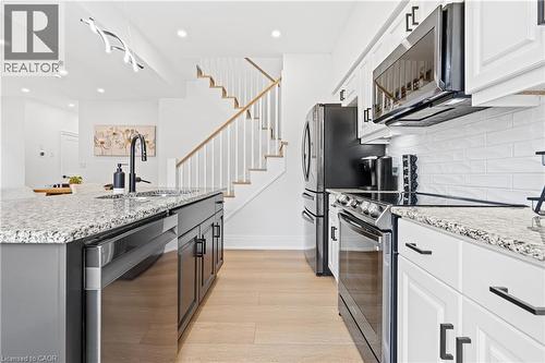 Modern kitchen featuring granite countertops, white cabinetry with black hardware, stainless steel appliances, and wood-finish flooring - 1026 Wright Drive, Midland, ON - Indoor Photo Showing Kitchen With Upgraded Kitchen