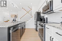Modern kitchen featuring granite countertops, white cabinetry with black hardware, stainless steel appliances, and wood-finish flooring - 