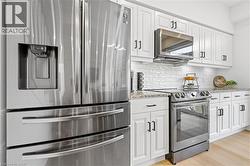 Modern kitchen featuring stainless steel appliances, white shaker-style cabinetry with dark hardware, a white subway tile backsplash, and light wood-finish flooring - 