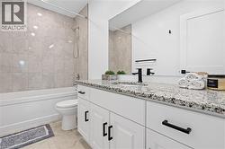 Bathroom featuring a white vanity with granite countertop, black fixtures, and a shower-tub combination with tile surround - 