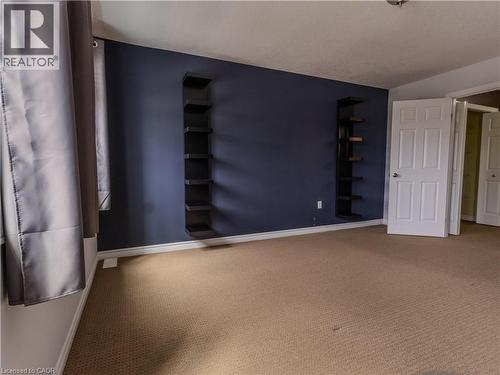 Spacious room featuring carpeting, dark blue accent wall with wall-mounted shelving, and white interior doors - 338 Maverick Street, Waterloo, ON - Indoor Photo Showing Other Room