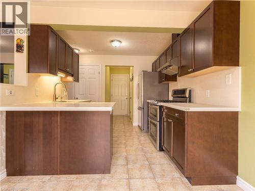 The kitchen features dark wood cabinetry, light-colored countertops, a stainless steel refrigerator, and a stainless steel range with a double oven - 338 Maverick Street, Waterloo, ON - Indoor Photo Showing Kitchen