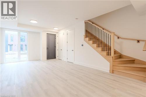 Bright open space featuring light-toned flooring, a light wood staircase with black metal balusters, and a large window - 144 Everett Common, St. Catharines, ON - Indoor Photo Showing Other Room
