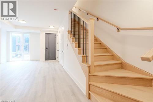 Entryway and living area featuring light-toned flooring, a light wood staircase with black metal balusters, a dark entry door, and a sliding glass door - 144 Everett Common, St. Catharines, ON - Indoor Photo Showing Other Room