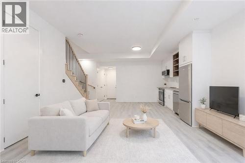 The property features light-toned flooring throughout, a modern staircase with dark balusters, and a kitchen area equipped with stainless steel appliances - 144 Everett Common, St. Catharines, ON - Indoor Photo Showing Living Room