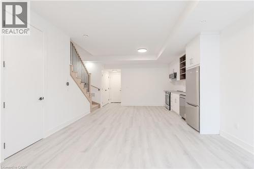 Open concept living space featuring light-toned flooring, a light wood staircase with dark balusters, and a compact kitchen area equipped with stainless steel appliances and white cabinetry - 144 Everett Common, St. Catharines, ON - Indoor