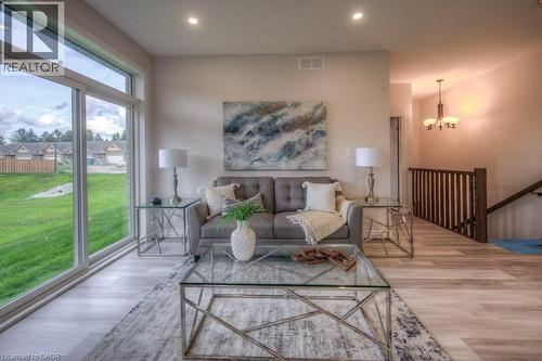 Bright living area featuring large sliding glass doors, light wood-finish flooring, recessed lighting, a modern staircase with dark wood railings, and a hanging chandelier - 48 Main Street E, Innerkip, ON - Indoor Photo Showing Living Room