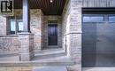 Brick and stone exterior featuring a covered porch, dark entry door, and modern garage door with integrated windows - 48 Main Street E, Innerkip, ON  - Outdoor 