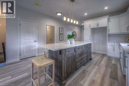 Open-concept kitchen featuring a large central island with a solid surface countertop, wood-finish flooring, recessed lighting, white cabinetry, and a built-in refrigerator enclosure - 48 Main Street E, Innerkip, ON - Indoor Photo Showing Kitchen