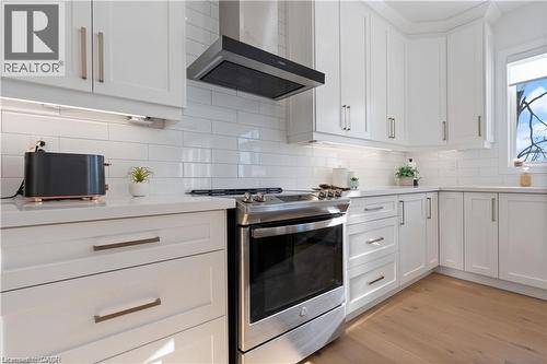 Kitchen with stainless steel gas range, white cabinetry, light wood-type flooring, backsplash, and light stone countertops - 66 Cesar Place, Ancaster, ON - Indoor Photo Showing Kitchen With Upgraded Kitchen