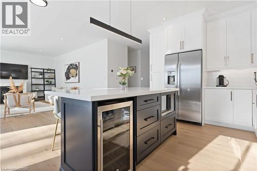 Dual tone kitchen featuring dual tone cabinetry, stainless steel refrigerator with ice dispenser, beverage cooler, light wood-style flooring, and a center island - 66 Cesar Place, Ancaster, ON - Indoor Photo Showing Kitchen