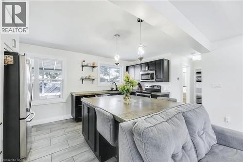 Open-concept kitchen featuring dark cabinetry, stainless steel appliances, a central island with seating, pendant lighting, and light-toned tile flooring - 18 Tweedsmuir Avenue, London, ON - Indoor Photo Showing Kitchen