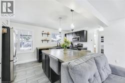 Open-concept kitchen featuring dark cabinetry, stainless steel appliances, a central island with seating, pendant lighting, and light-toned tile flooring - 