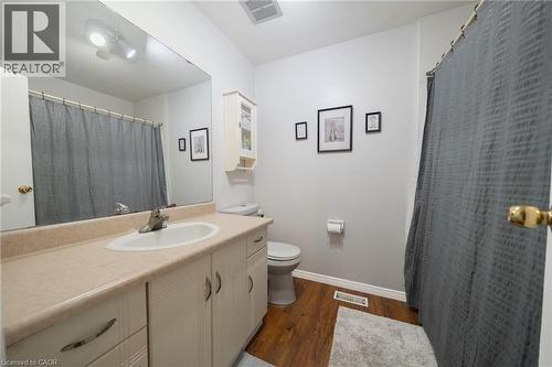 Bathroom featuring a vanity with an integrated sink, a large wall mirror, wood-finish flooring, a built-in wall cabinet, and an overhead light fixture - 391 Pioneer Drive Unit# 4, Kitchener, ON - Indoor Photo Showing Bathroom