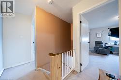 Upper-level landing featuring light-colored carpeting, a light wood-finish stair railing with white spindles, a painted accent wall, and a ceiling-mounted smoke detector - 