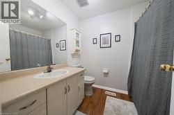 Bathroom featuring a vanity with an integrated sink, a large wall mirror, wood-finish flooring, a built-in wall cabinet, and an overhead light fixture - 
