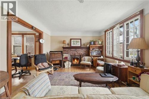 Living room featuring wood-finish flooring, a brick fireplace with a wood mantle, and white-framed windows with dark wood trim - 509 Aberdeen Avenue, Hamilton, ON - Indoor Photo Showing Living Room With Fireplace