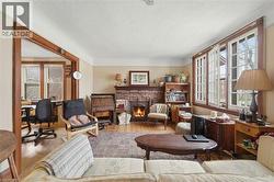 Living room featuring wood-finish flooring, a brick fireplace with a wood mantle, and white-framed windows with dark wood trim - 