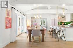 Open-concept dining area and kitchen featuring light wood-finish flooring, a vaulted ceiling with exposed beams, and a breakfast bar with seating - 